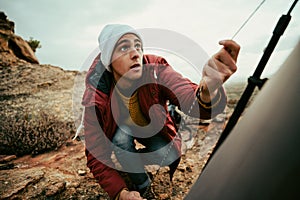 Caucasian male concentrating puling ropes to tie tent camping on top of mountain