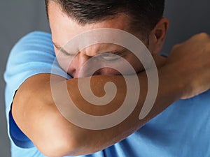 Caucasian male coughs in his elbow.