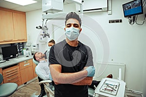 Caucasian male dentist wearing surgical mask and gloves standing by female dentist ready to operate