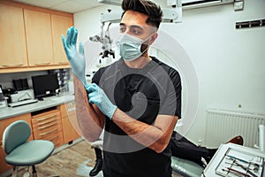 Caucasian male doctor wearing surgical mask and gloves standing in doctors office ready to operate