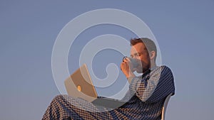 Caucasian male drinking coffee or tea outdoor in nightwear using laptop, 4K