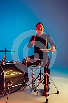 Caucasian male drummer improvising isolated on blue studio background in neon light