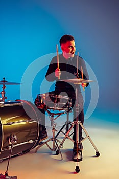 Caucasian male drummer improvising isolated on blue studio background in neon light