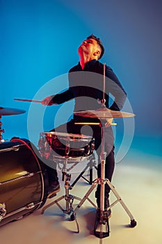 Caucasian male drummer improvising isolated on blue studio background in neon light