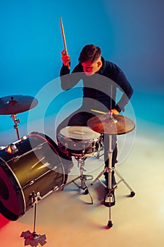 Caucasian male drummer improvising isolated on blue studio background in neon light