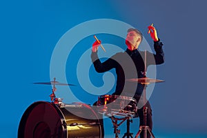 Caucasian male drummer improvising isolated on blue studio background in neon light