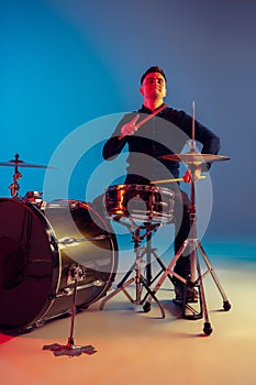 Caucasian male drummer improvising isolated on blue studio background in neon light