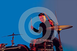 Caucasian male drummer improvising isolated on blue studio background in neon light