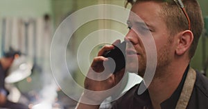 Caucasian male factory worker at a factory standing in a workshop, talking on a smartphone