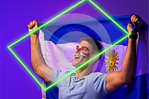 Caucasian male fan with argentina national flag and face paint screaming by illuminated rectangle