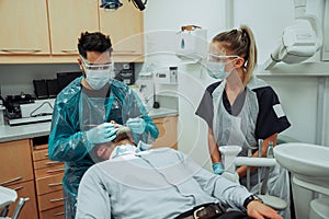 Caucasian male and female dentists standing in doctors room while operating on male clients teeth