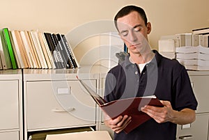 Caucasian male in file room reading papers inside a folder