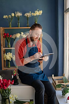Caucasian male flower shop owner wearing apron holding clipboard in hands while taking inventory