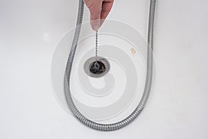 Caucasian male hand holding a bathtub rubber plug on a chain next to shower cord close up shot top view