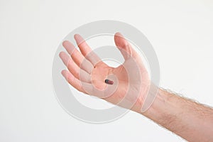Caucasian male hand holding a medical black and red capsule pill in his palm. Close up studio shot, isolated on white background