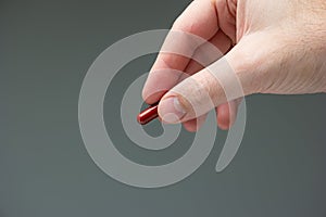 Caucasian male hand holding a red medicine capsule pill between fingers close up shot isolated studio shot