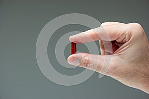 Caucasian male hand holding a red medicine capsule pill between fingers close up shot isolated studio shot