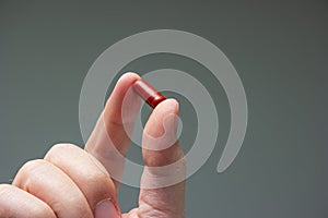 Caucasian male hand holding a red medicine capsule pill between fingers close up shot isolated studio shot