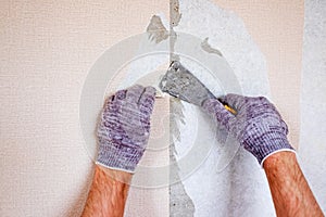 Caucasian male hands tearing off old wallpaper from wall preparing for home redecoration