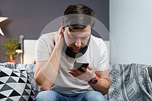 Caucasian male has neck injury to relieve pain, puts on cervical brace made of soft black cotton, male uses smartphone at home