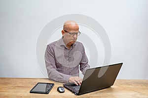 Caucasian male middle aged and with glasses, sitting behind a desk working with his lap top