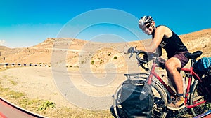 Caucasian male person stand by bicycle solo touring in tranquil countryside fully loaded with bags outdoors in summer heat.