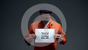 Caucasian male prisoner holding They wanna kill me sign, calling for help