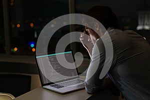 Caucasian male programmer sitting at desk, using laptop with coding on screen