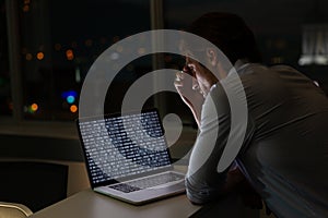 Caucasian male programmer sitting at desk, using laptop with coding on screen
