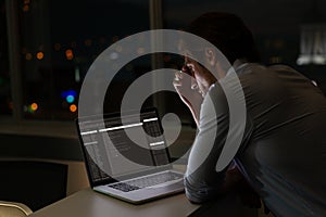 Caucasian male programmer sitting at desk, using laptop with coding on screen
