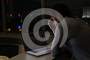 Caucasian male programmer sitting at desk, using laptop with coding on screen