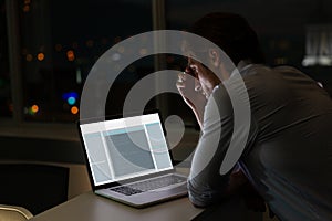 Caucasian male programmer sitting at desk, using laptop with coding on screen