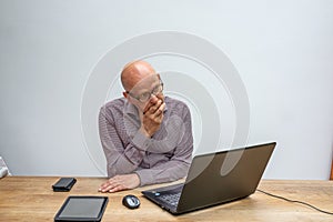 Caucasian male sitting behind a desk with lap top talking into a cell phone