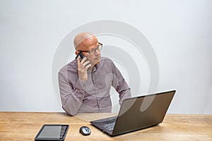 Caucasian male sitting behind a desk with lap top talking into a cell phone