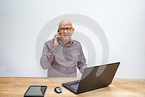 Caucasian male sitting behind a desk with lap top talking into a cell phone