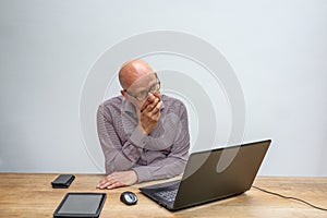 Caucasian male sitting behind a desk with lap top talking into a cell phone
