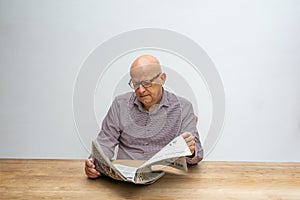 Caucasian male sitting behind a desk reading the news paper whilst drinking a cup of coffee