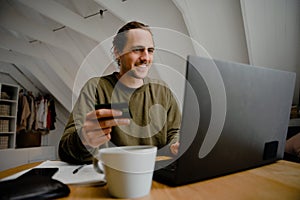 Caucasian male student smiling while sitting at desk successfully affording monthly rent enjoying hot coffee photo