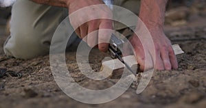 Caucasian male survivalist cutting notch in fireboard at camp in wilderness