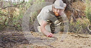 Caucasian male survivalist squatting down and examining animal dropping in wilderness