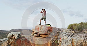 Caucasian male survivalist using binoculars, standing on mountain peak in wilderness