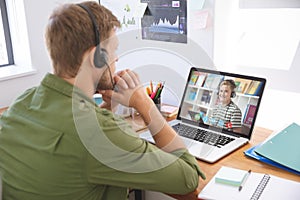 Caucasian male teacher using computer and phone headset on video call with schoolboy