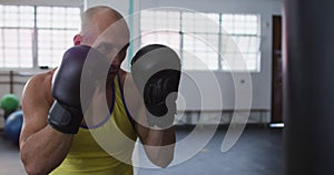 Caucasian male trainer wearing boxing gloves training with punching bag at the gym