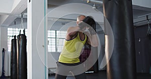 Caucasian male trainer wearing boxing gloves training with punching bag at the gym