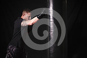 Caucasian male wearing a black t-shirt, punching a hanging boxing bag in a gym setting