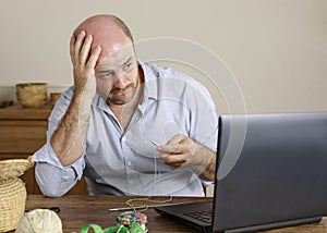 Caucasian man, 30-39 years old, grabbing his head in frustration, while looking at the computer and trying to knit with two