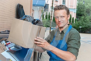 Caucasian Man in apron is Throwing Away paper box and plastic bag of Trash. Man taking out big paper box on trash into