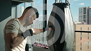 Caucasian man athlete boxer training with punching bag in modern fitness gym strong powerful sportsman fighter boxing
