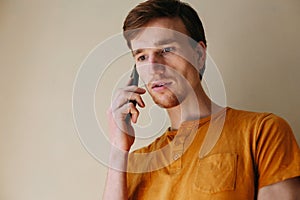 Caucasian man with beard in casual orange shirt talking with mobile phone in living room about serious problem