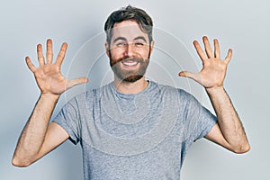 Caucasian man with beard wearing casual grey t shirt showing and pointing up with fingers number ten while smiling confident and